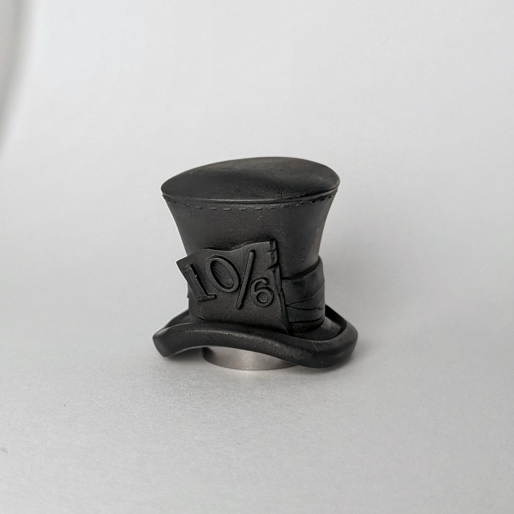 The Mad Hatter's hat as a perfume bottle cap, with stitching detail, folded fabric detailing, and a 10/6 card.