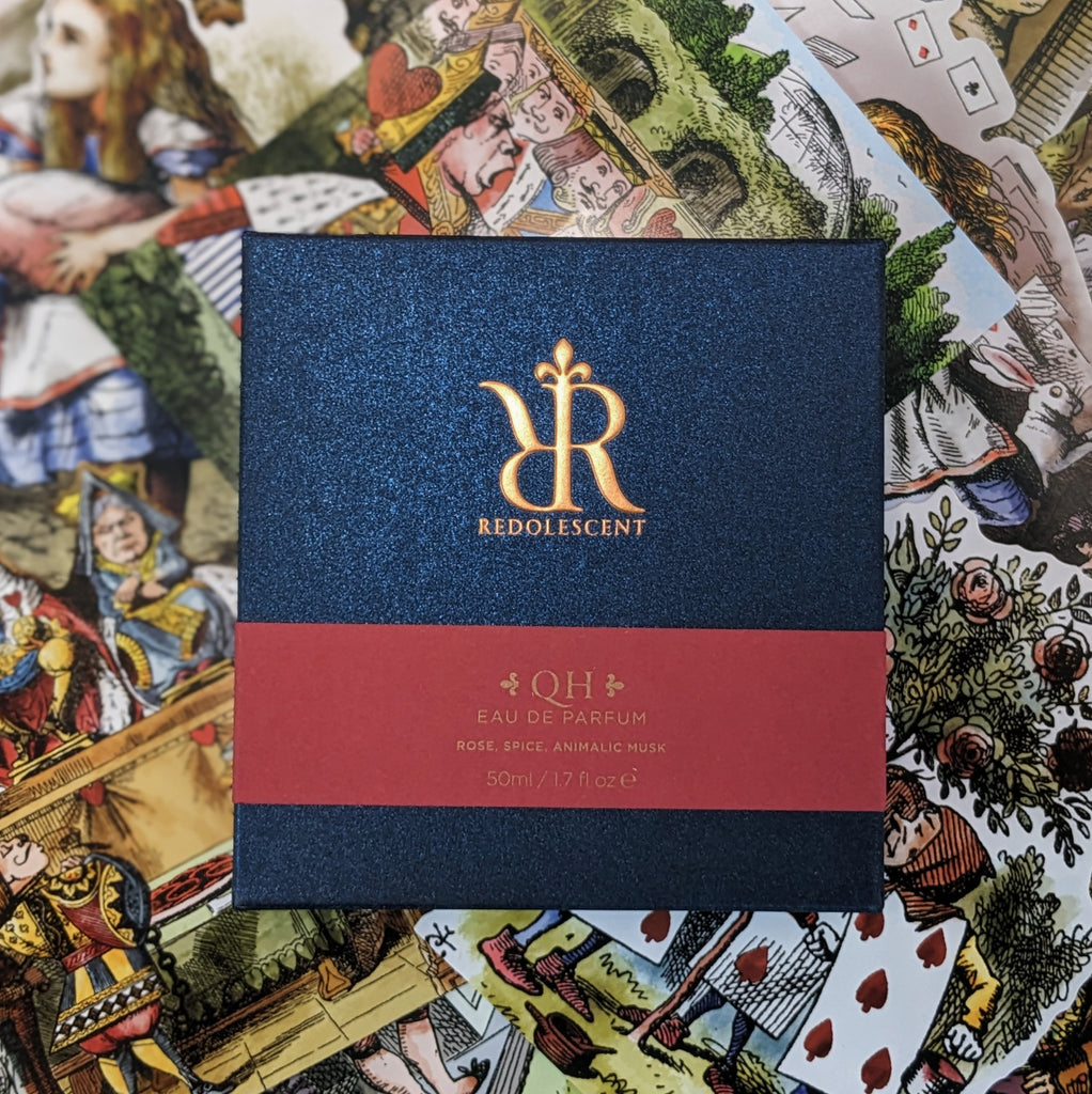Packaging for QH. A blue box with a red band across the middle. The box has a copper foil Redolescent logo, while the band has copper ink "QH, Eau de Parfum" "Rose, spice, animalic musk".